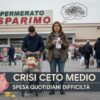 Una donna preoccupata guarda lo scontrino della spesa nel parcheggio di un supermercato, mentre un ragazzo spinge il carrello pieno.